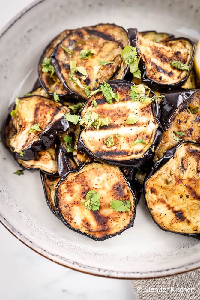 Garlic grilled eggplant with grill marks in a bowl with parsley and lemon.