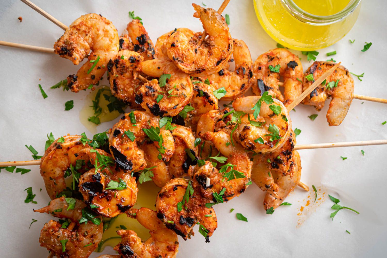 Grilled garlic shrimp skewers with melted butter, lemon, and minced parsley on parchment paper.