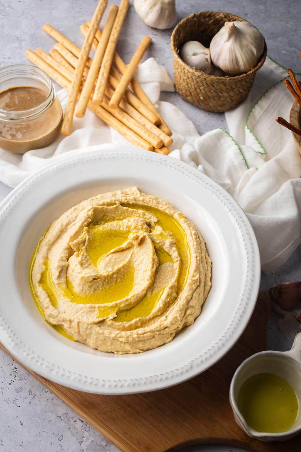 Roasted garlic hummus made with chickpeas, tahini, and lemon in a bowl with breadsticks.