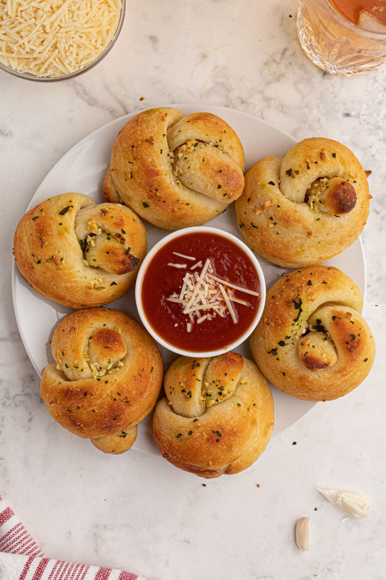 Two ingredient dough garlic knots on a plate with marinara sauce and Parmesan cheese for dipping.