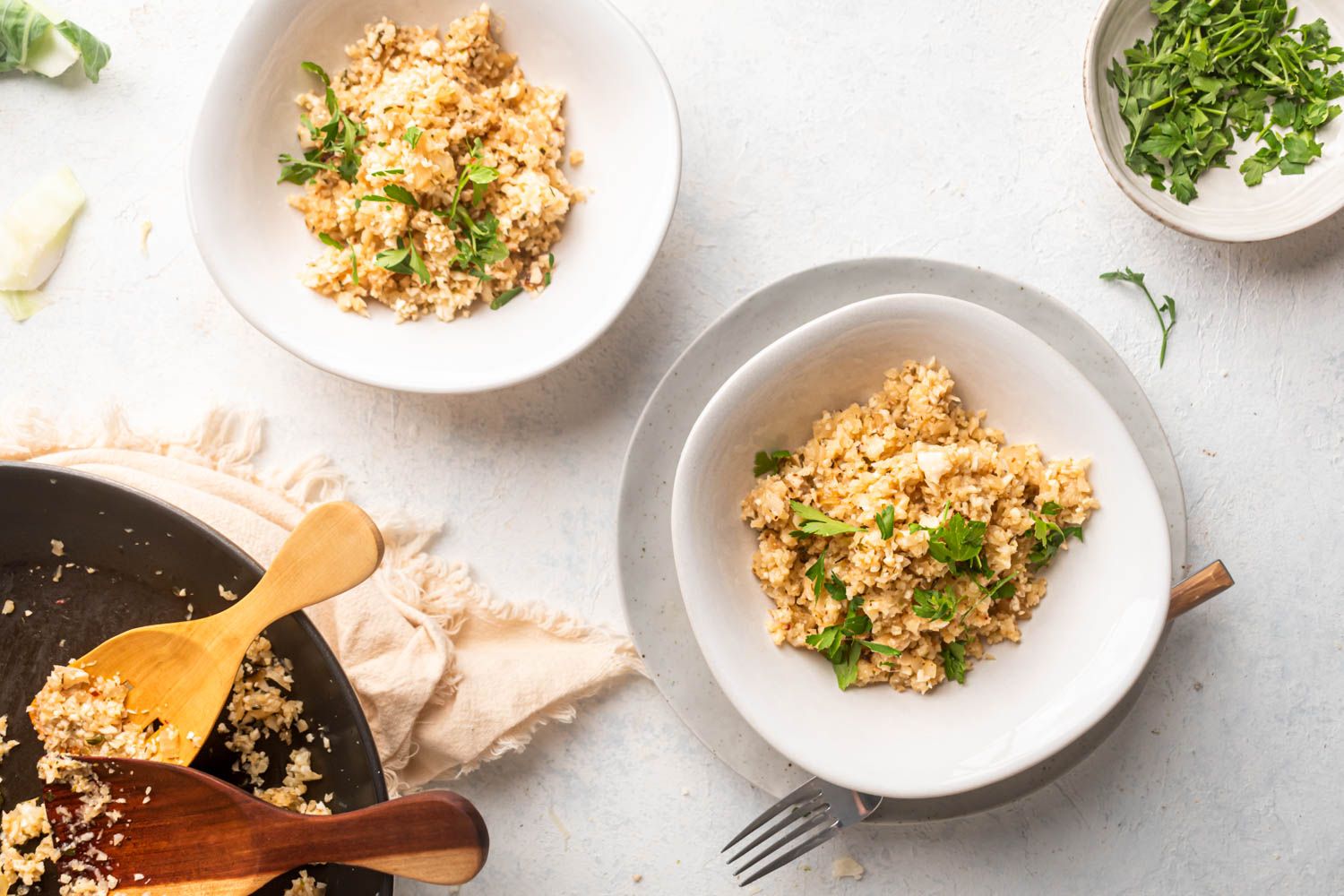 Low carb garlic cauliflower rice with Parmesan cheese and parsley served in two bowls and a skillet.