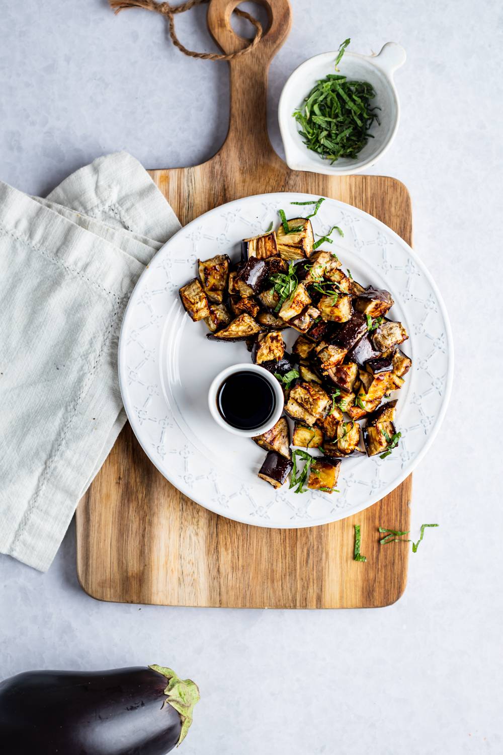 Roasted eggplant with caramelized edges served on a plate with fresh basil and balsamic vinegar.