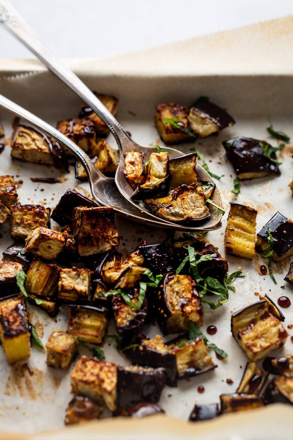 Cubes of roasted eggplant with balsamic glaze, garlic, and herbs on a baking sheet.