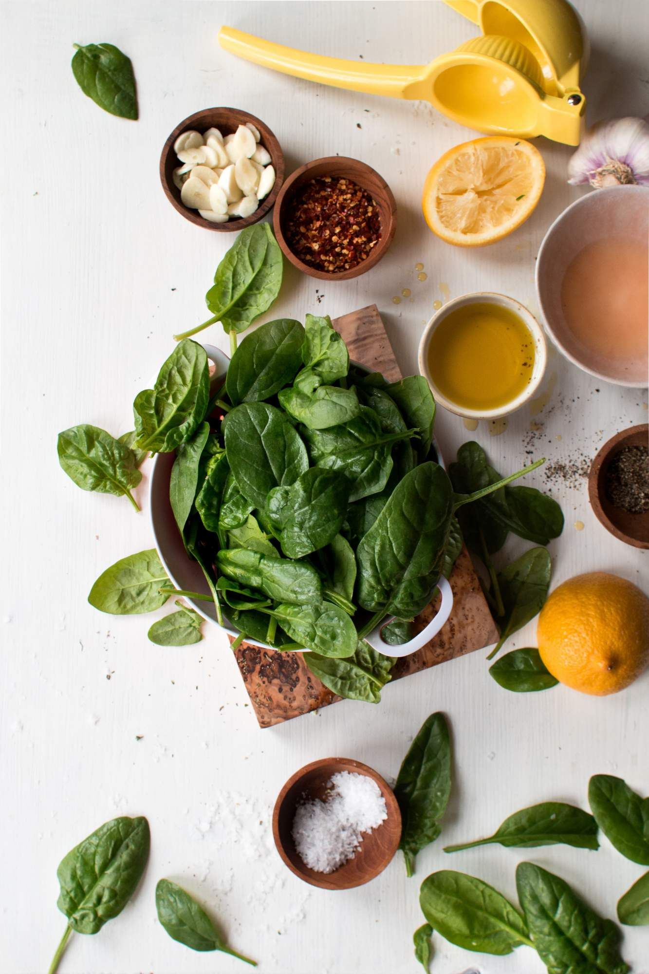 Ingredients for sauteing spinach including baby spinach, garlic, olive oil, lemon juice, salt, and pepper.