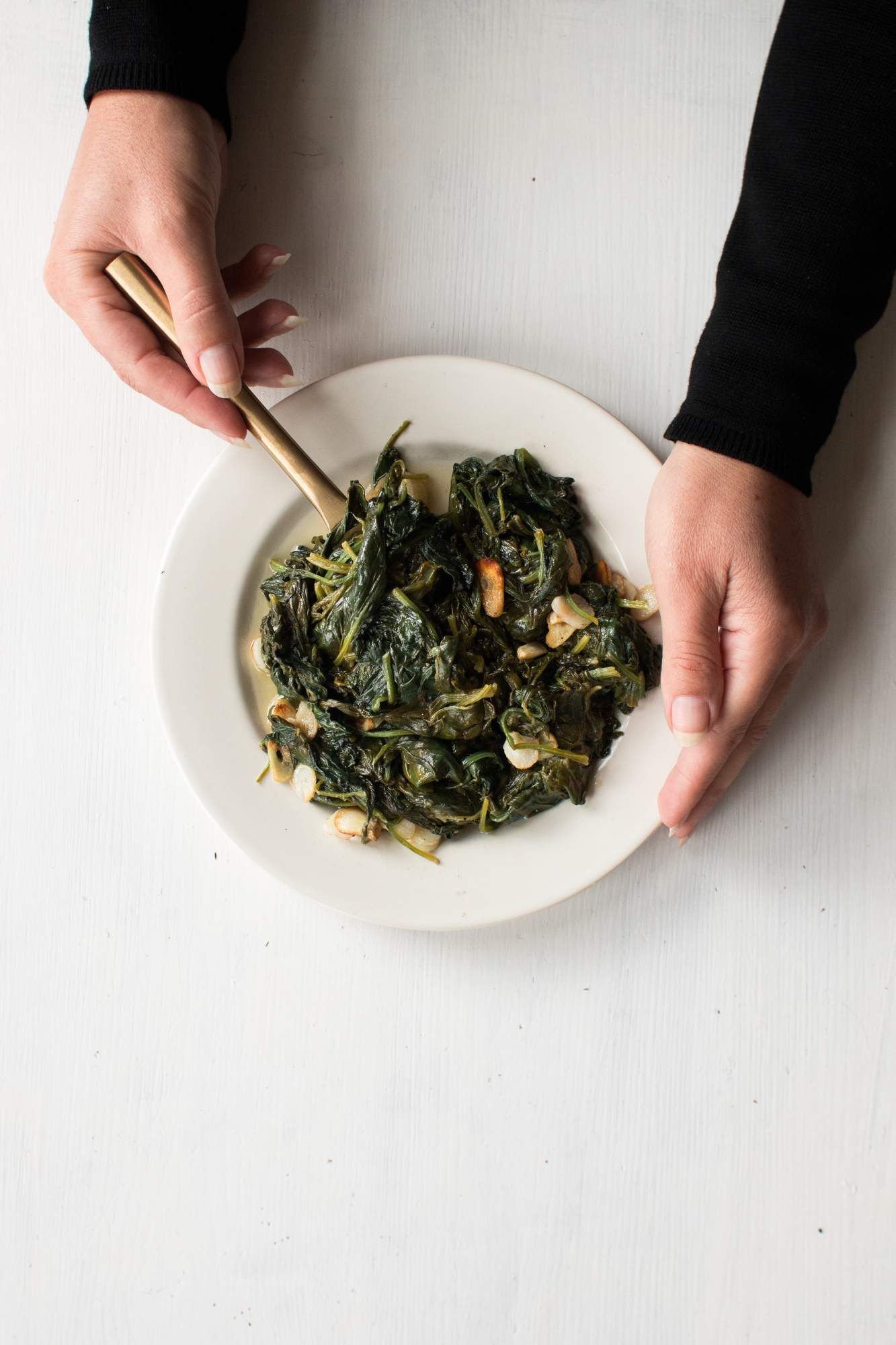 Sautéed spinach with garlic and lemon in a dish being held by two hands. 