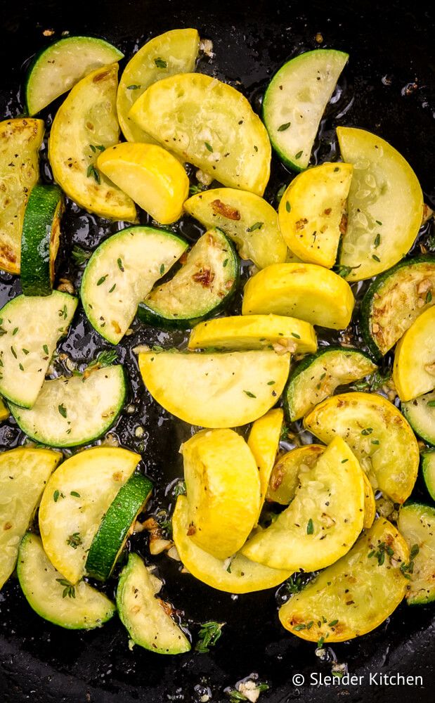 Garlic sauteed zucchini and squash in a black skillet with fresh thyme.