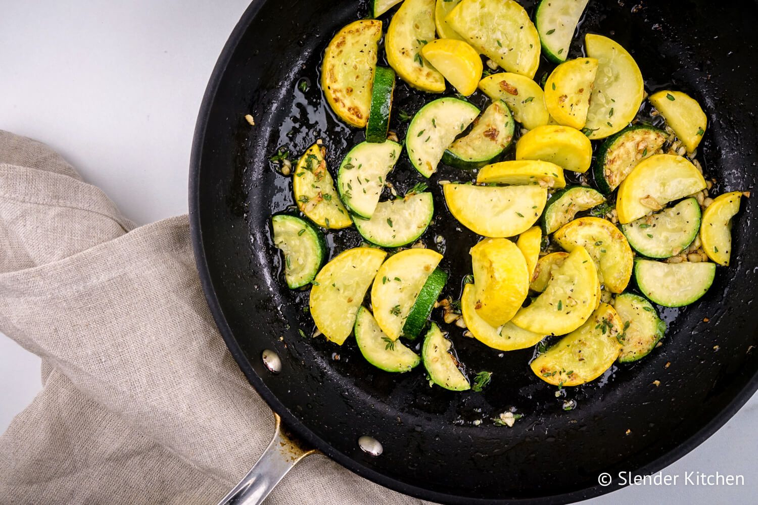 Sauteed zucchini with garlic, thyme, and summer squash in a skillet.