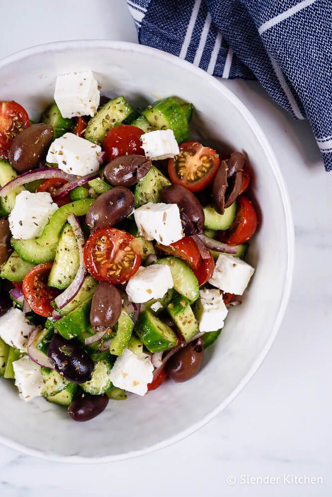 Authentic Greek salad with cucumbers, tomatoes, green pepper, olives, feta cheese, red onion, and oregano in a bowll. 