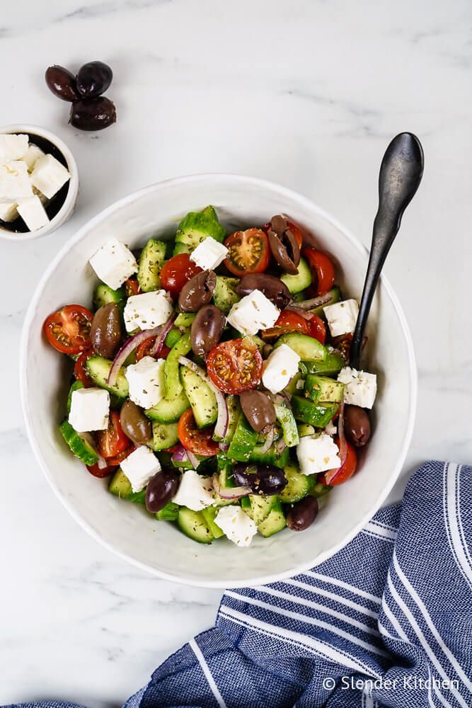 Greek salad with black olives, feta cheese, tomatoes, cucumbers, red onion, green pepper, and Greek dressing in a bowl with a fork.