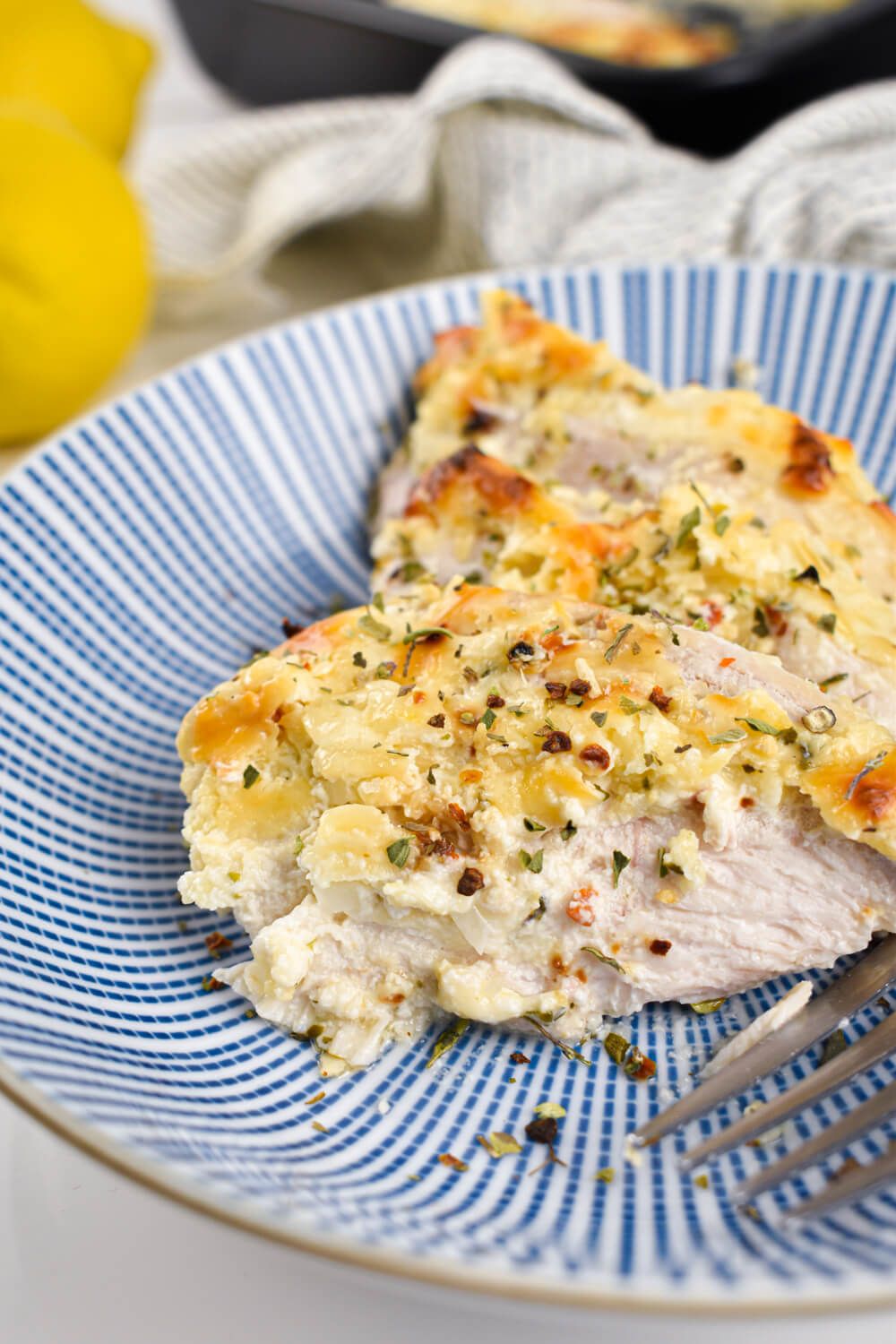 Chicken in Parmesan Greek Yogurt Sauce on a plate with herbs, fresh lemons, and a napkin.