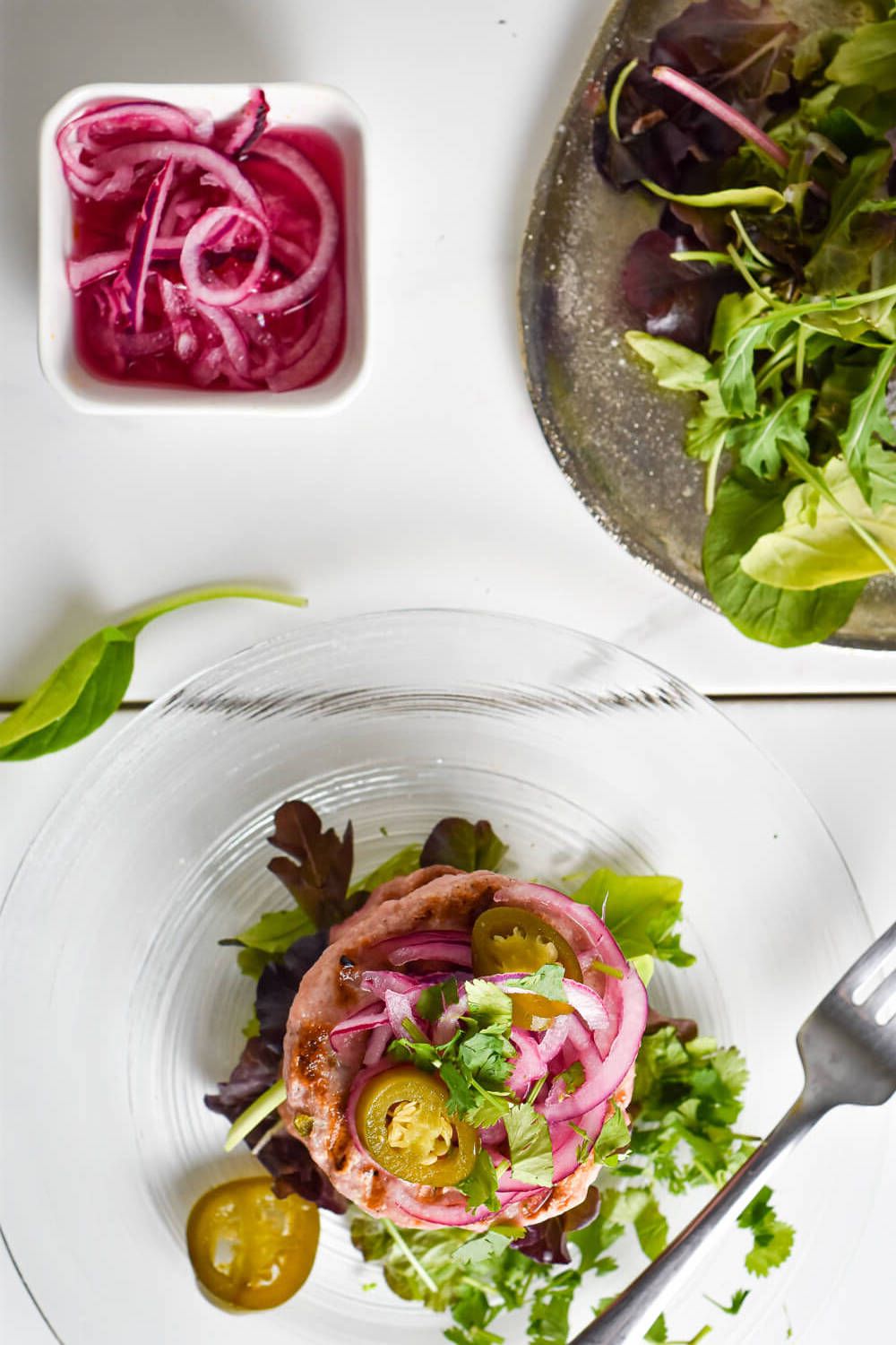 Turkey burgers with green chilies and red onions on a plate of lettuce.