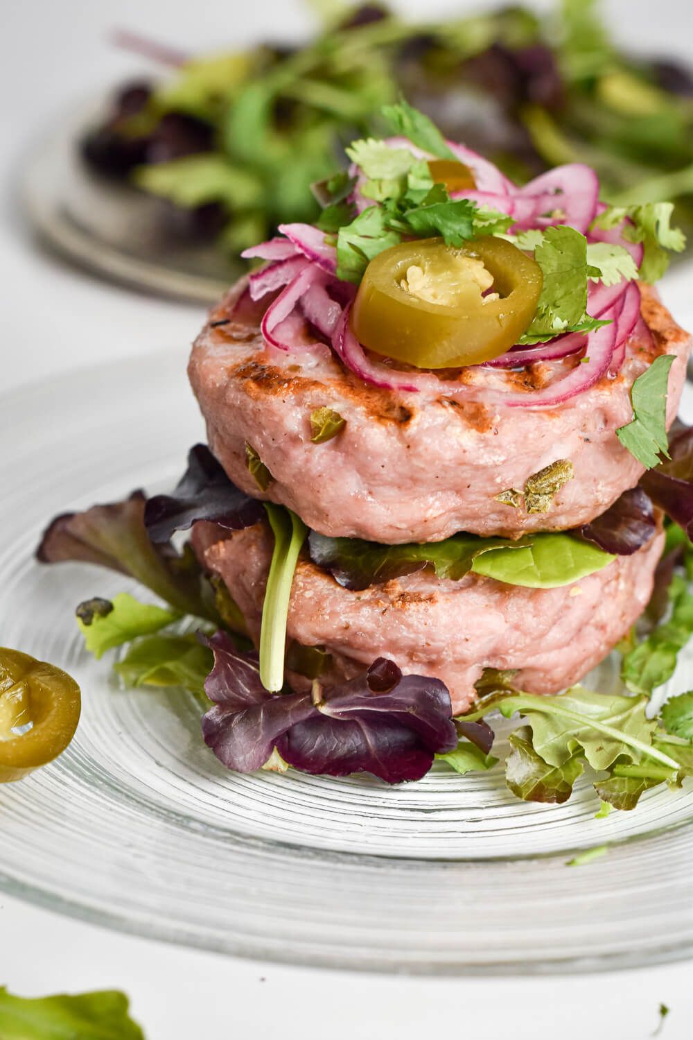 Spicy turkey burgers with green chilies, pickled red onions, and lettuce on a clear plate.