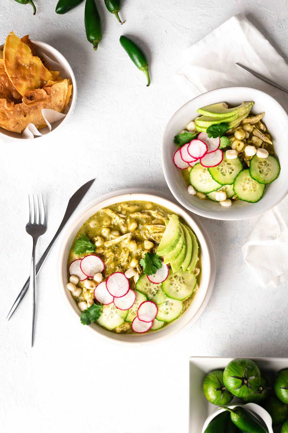 Green chicken pozole in two bowls with shredded chicken, hominy, green broth, abocado, and sliced radishes.