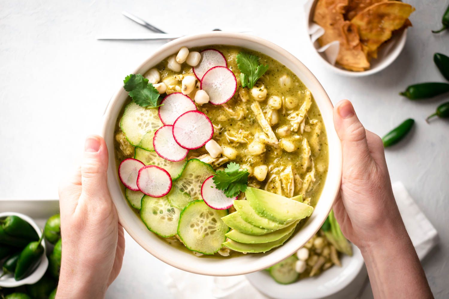 Pozole verde with chicken in a bowl with radishes, cilantro, avocado, hominy, and cucumbers.