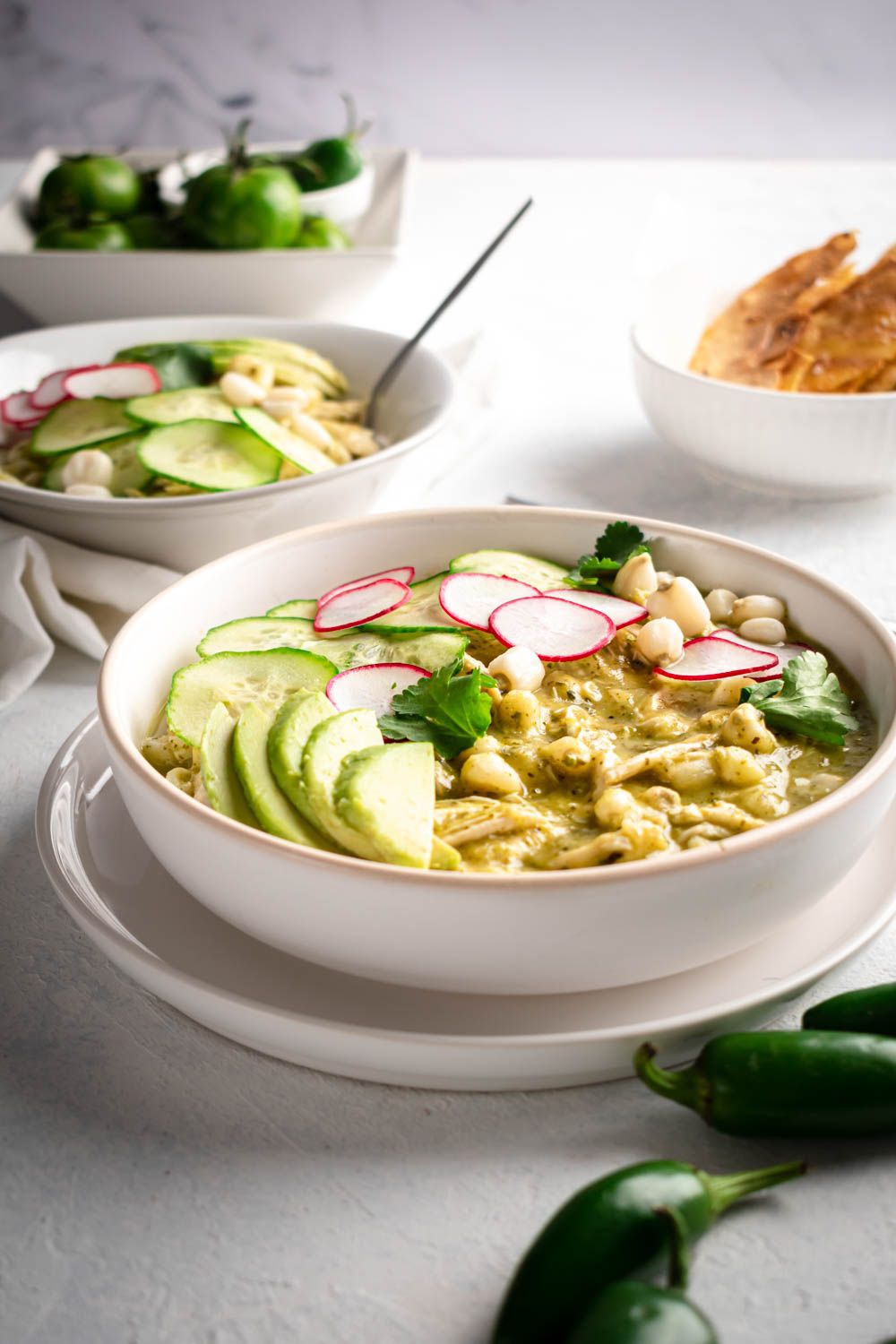 Mexican pozole verde with shredded chicken and hominy in two bowls with jaalpeno, cilantro, and radishes.