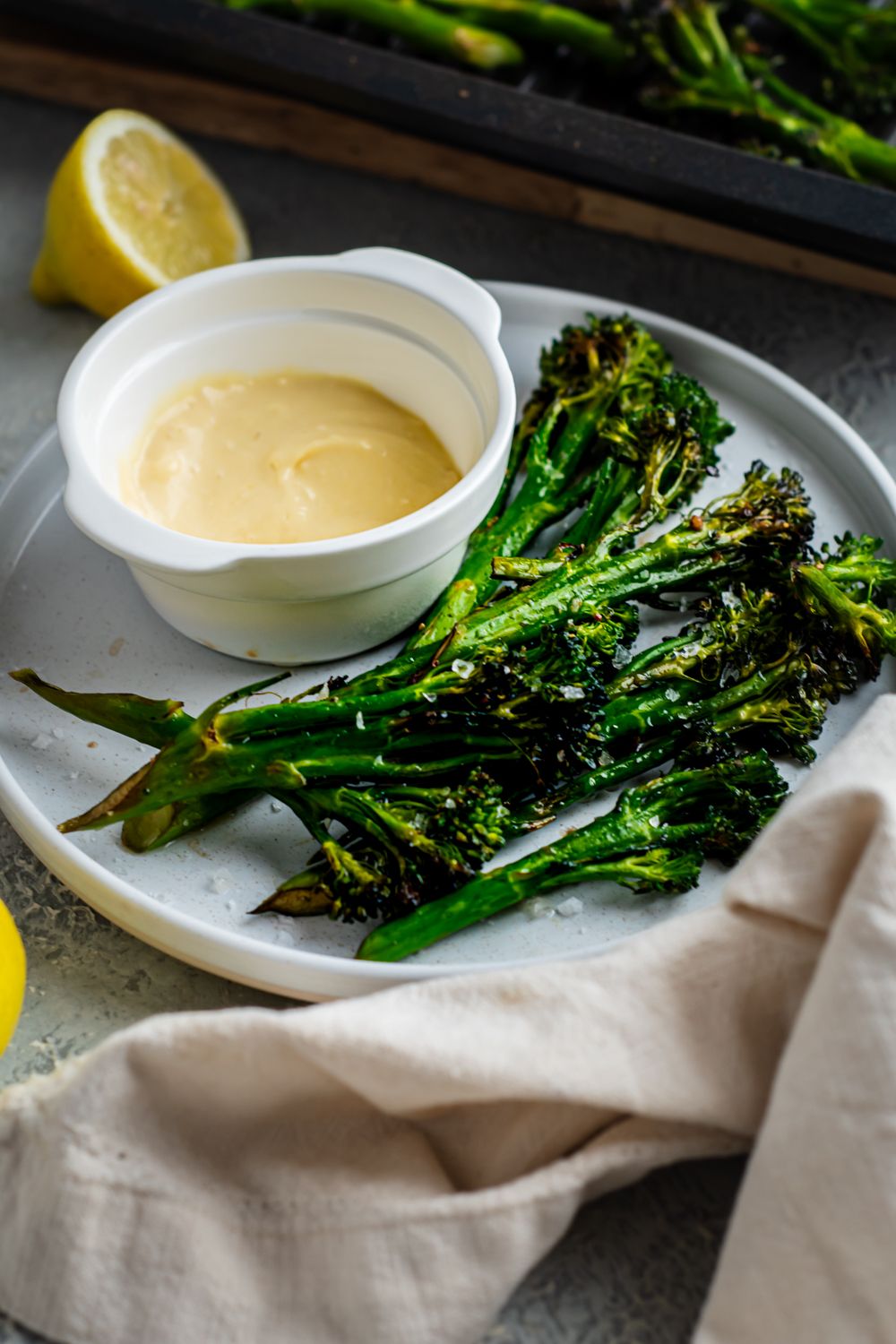 Grilled broccolini with charred edges served on a plate with lemon and garlic dipping sauce.