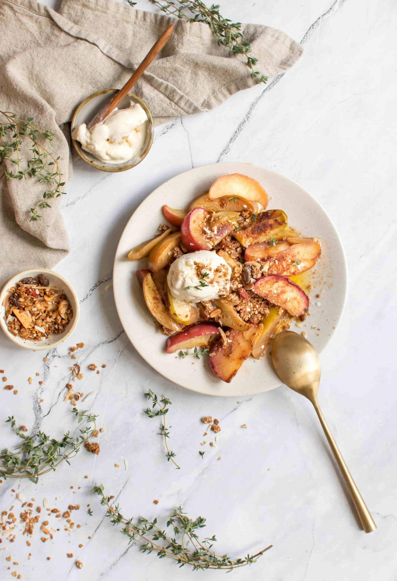 Grilled apples on a plate with yogurt, granola, and thyme with a cloth napkin.