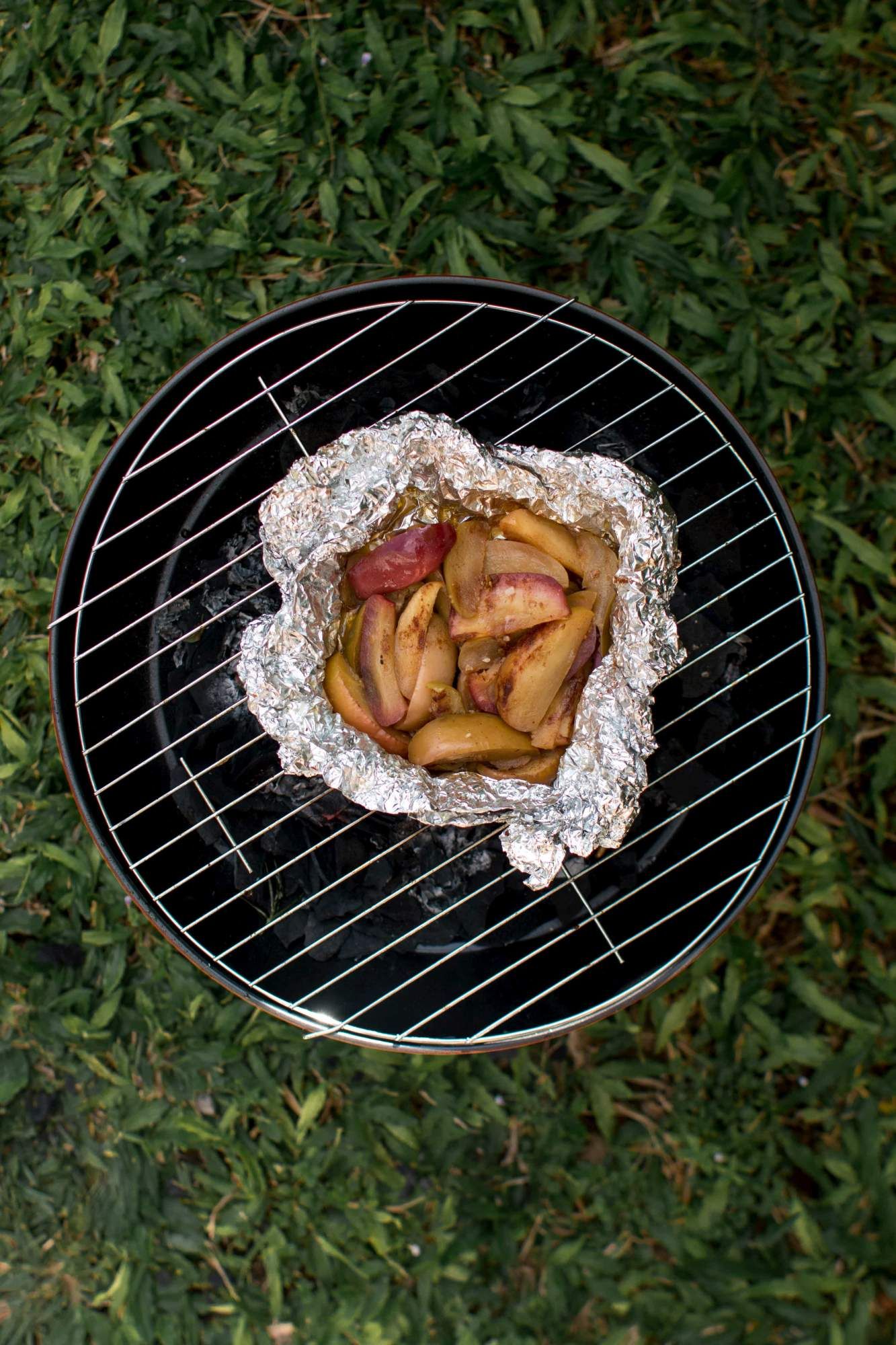 Apples being grilled on an outdoor grill with grass in the background.