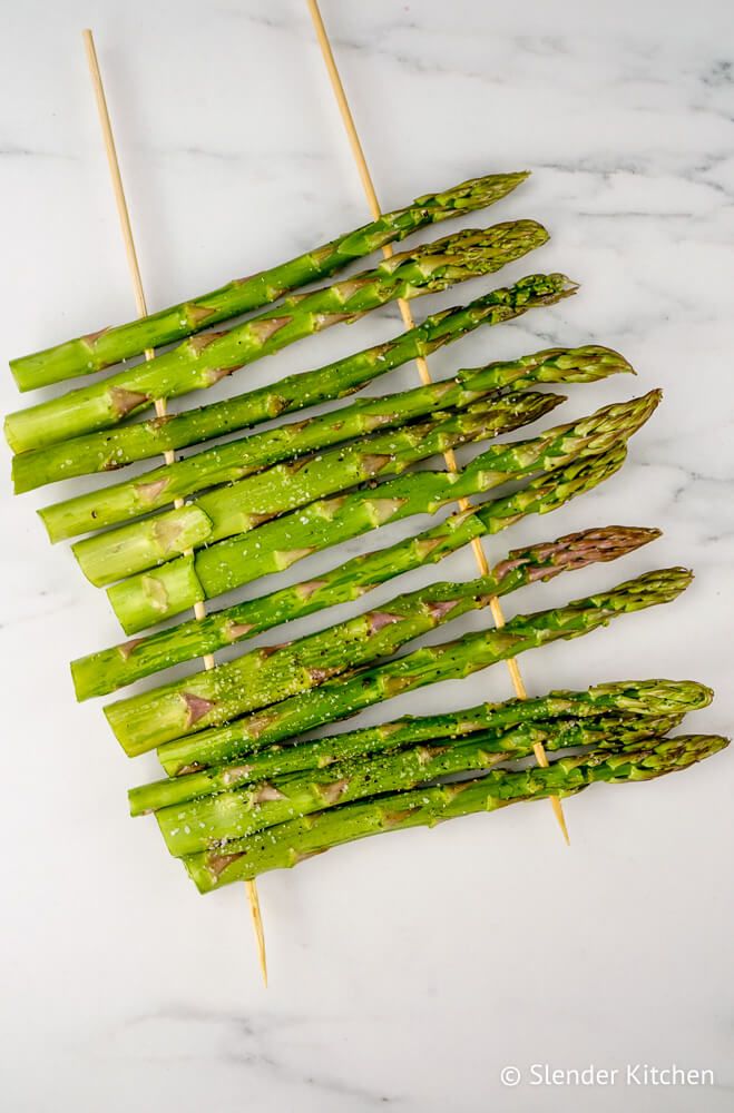 Grilled asparagus on wooden skewers before being cooked.