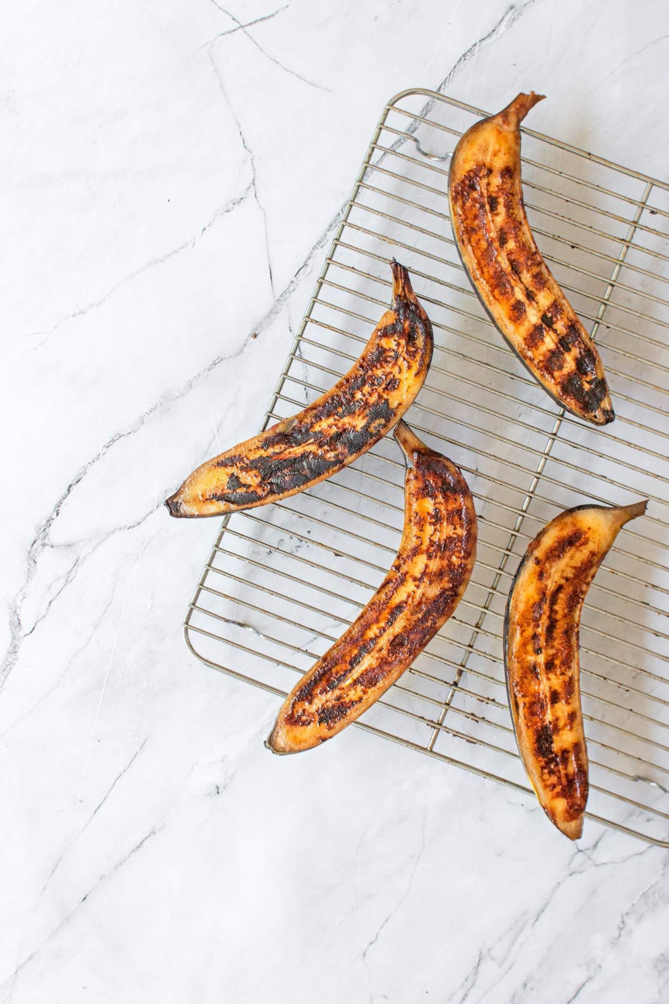 Bananas that have been grilled on a wire rack with grill marks and caramelized edges. 