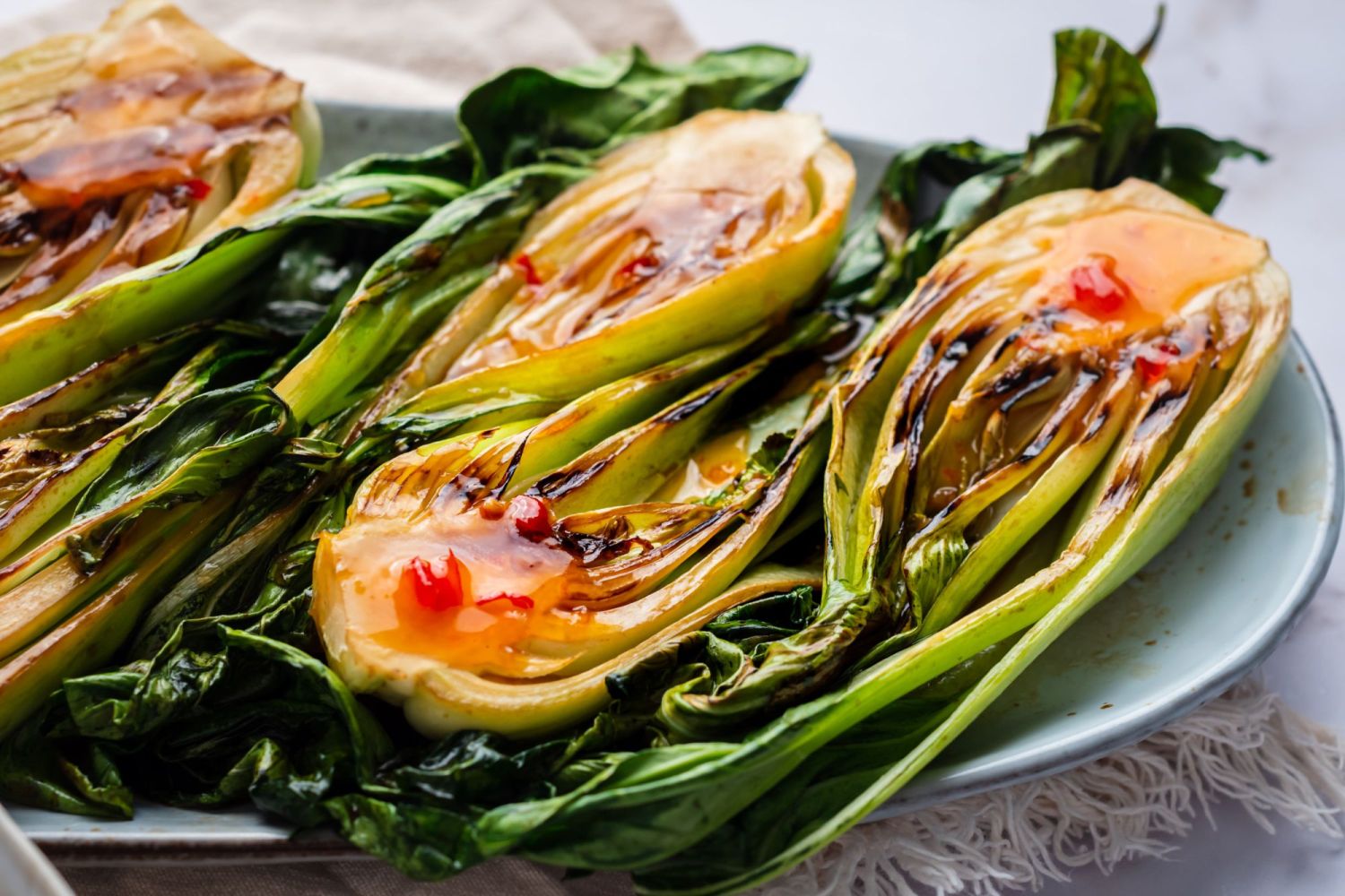 Baby bok choy cooked on the grill and served on a plate with Thai chili sauce and soy sauce.