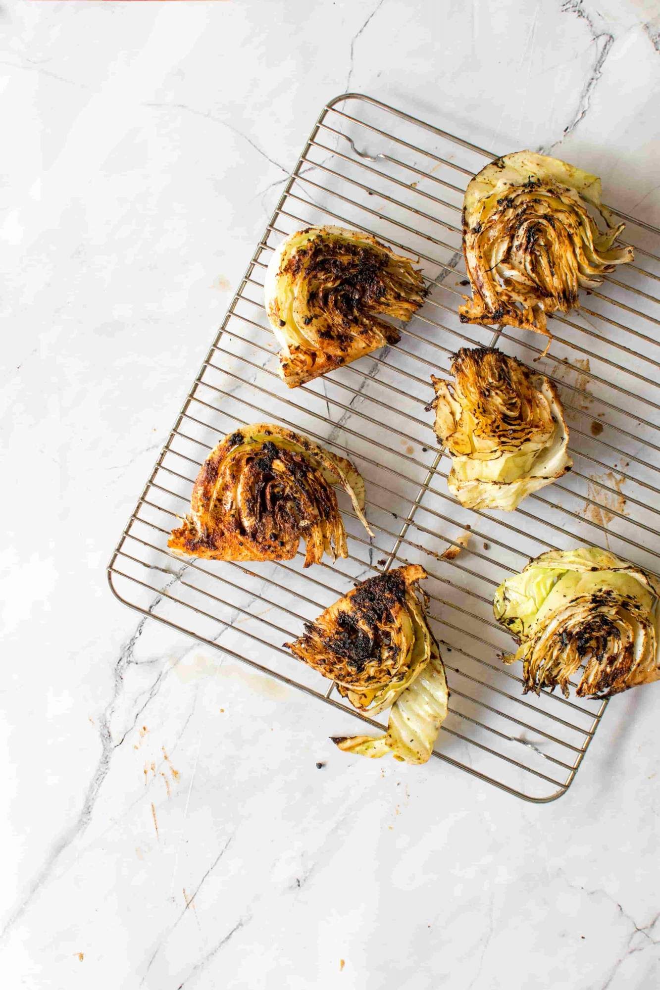 Sliced cabbage with grill marks, crispy browned edges, and spices on a wire rack.