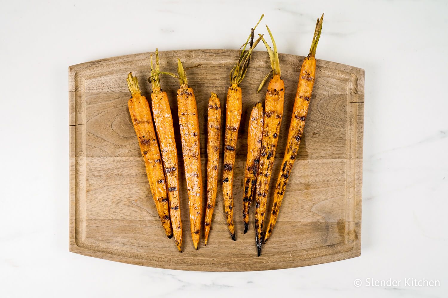 Grilled carrots on a cutting board with grill marks and a sprinkle of salt and pepper.