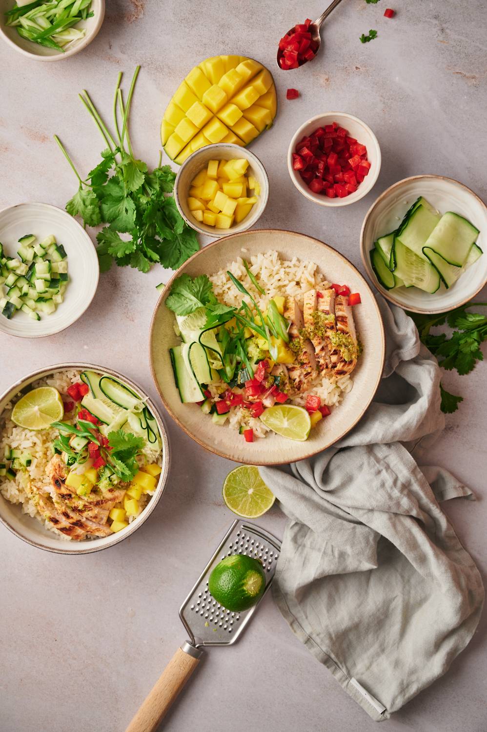 Grilled chicken and white rice bowls with mango salsa, cucumbers, and cilantro in a bowl with extra toppings on the side.