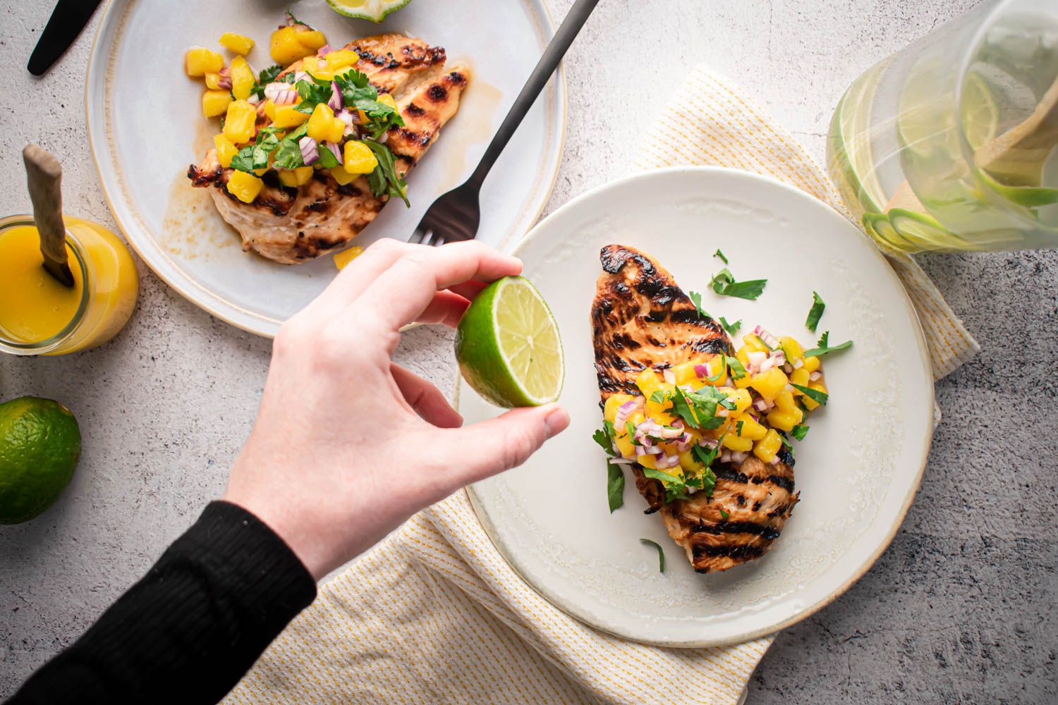 Mango salsa grilled chicken served on a plate with grilled chicken breast topped with mango, cilantro, and red onion.