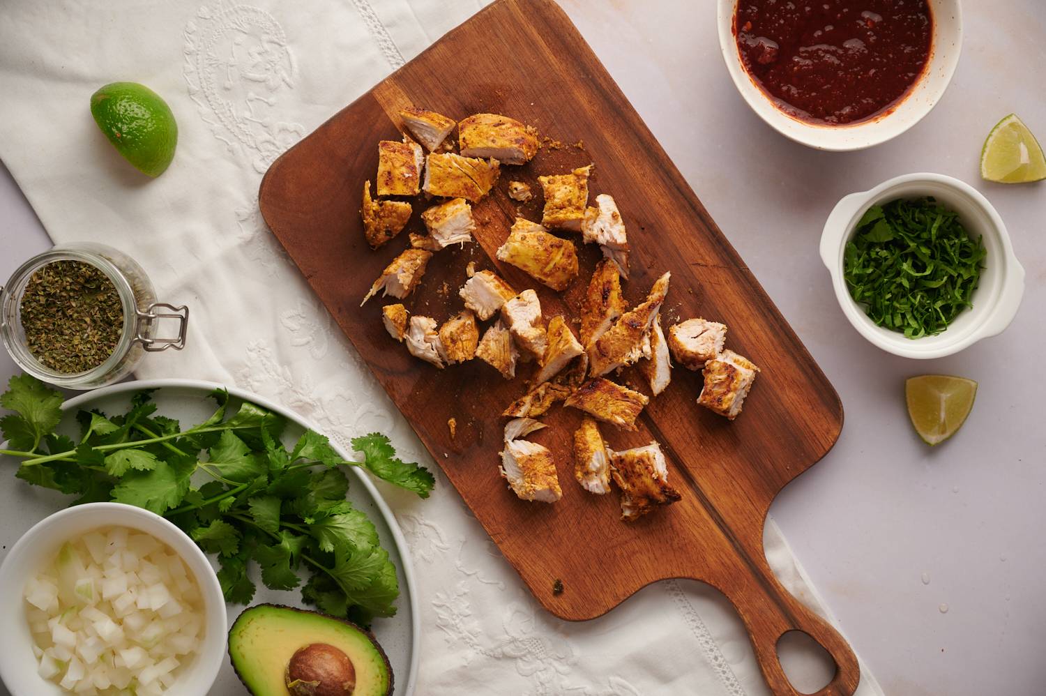 Grilled chicken on a chopping board for chicken tacos with salsa, cilantro, limes, and onion on the side.