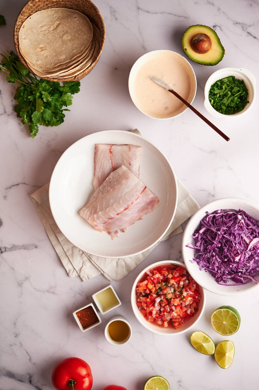 Ingredients for grilled fish tacos including white fish, tortillas, cabbage, pico de gallo, taco seasoning, and avocado.