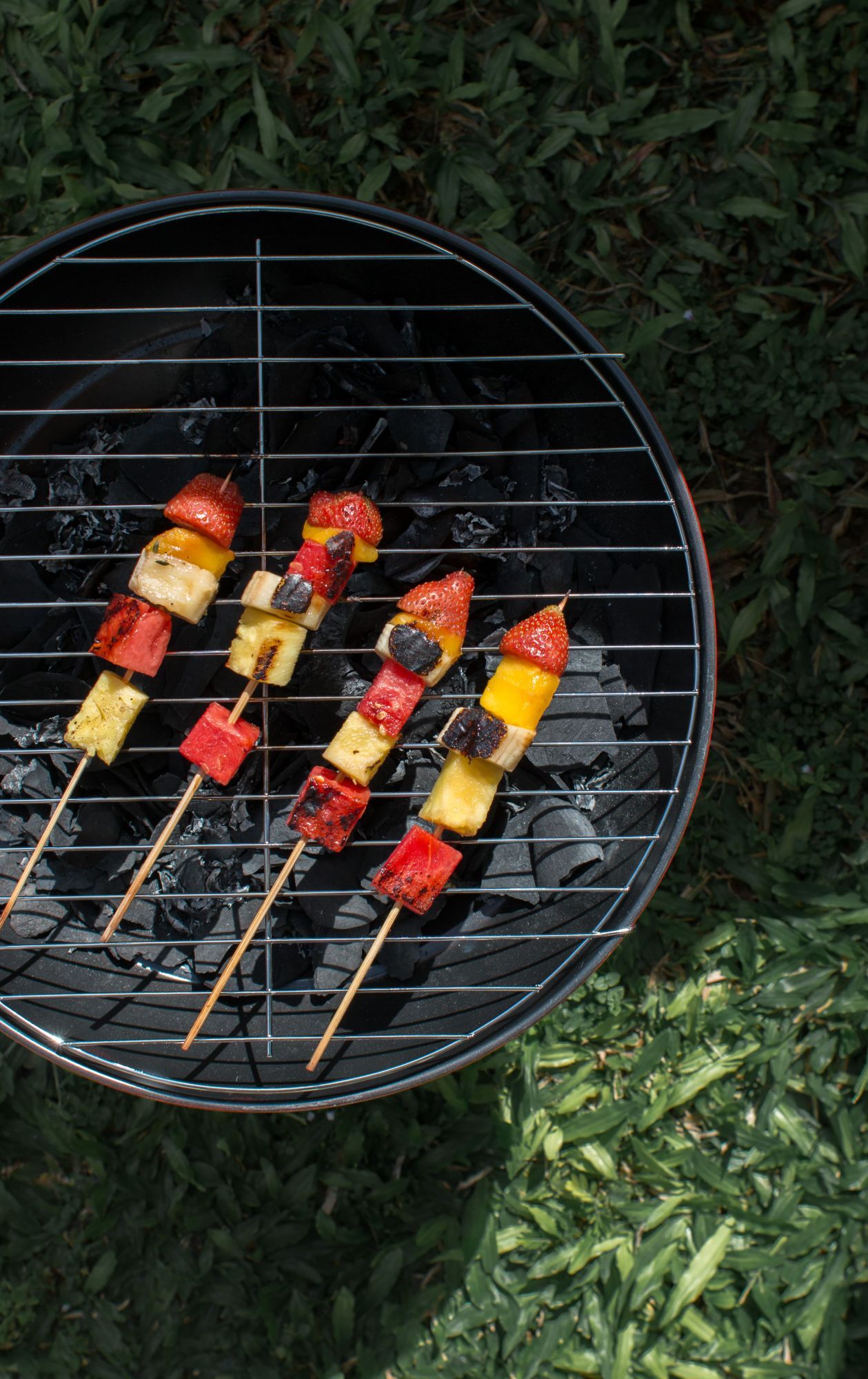 Grilled kabob with various fruit on an outdoor charcoal grill.