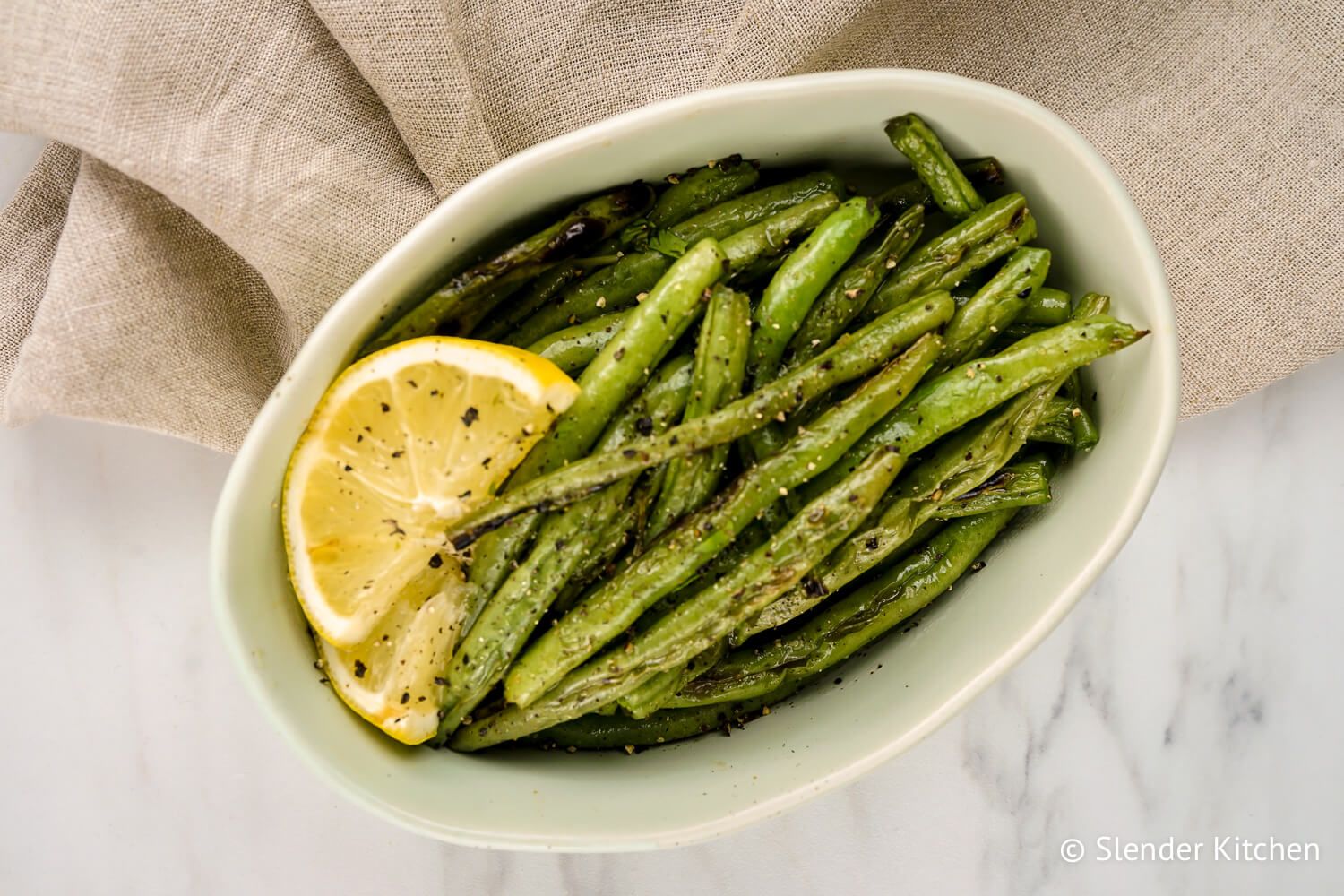 Green beans grilled with lemon slices, salt, and pepper in a white dish.