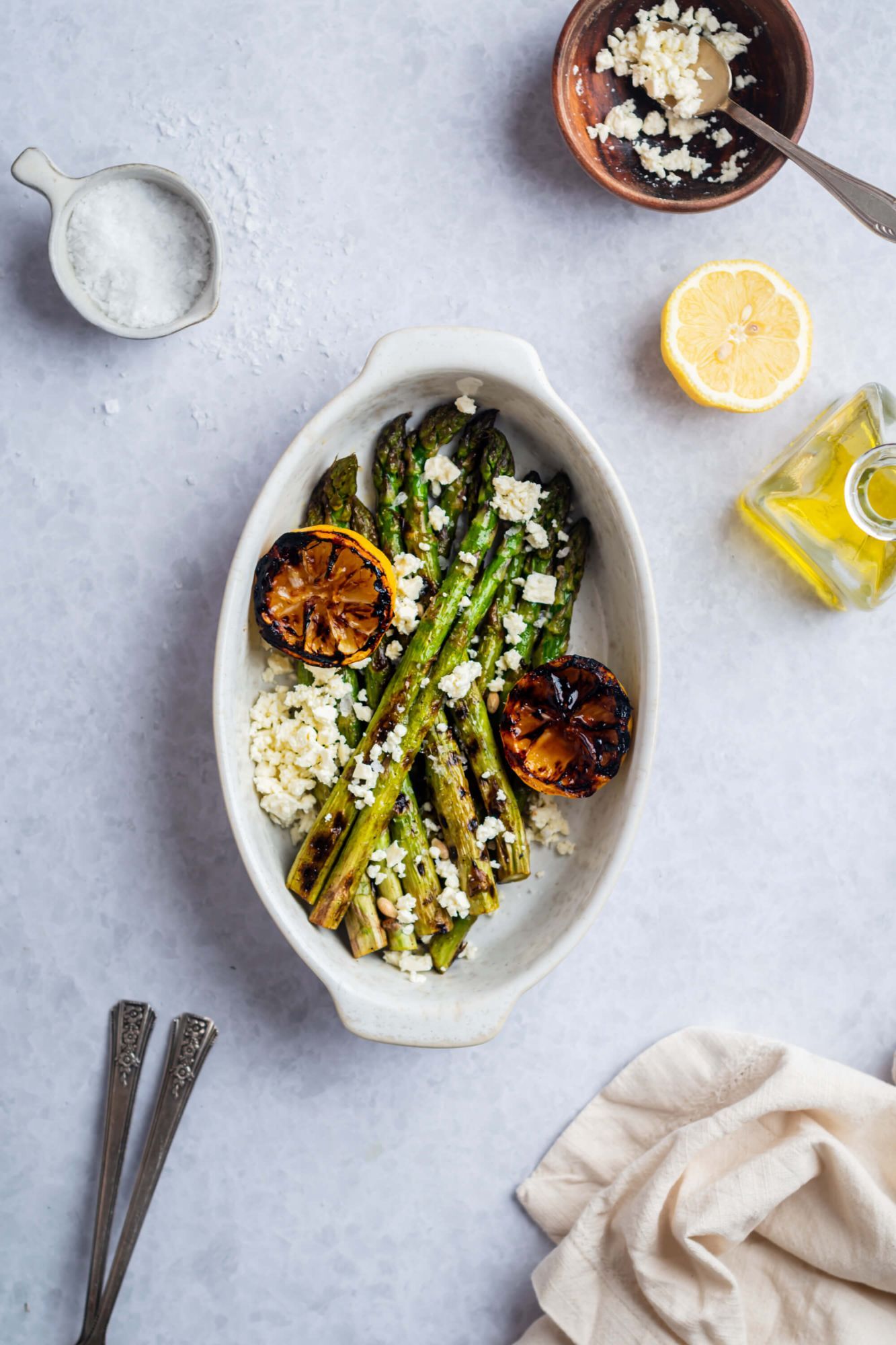 Grilled asparagus with grilled lemons and feta cheese in a dish with extra feta and lemon on the side.