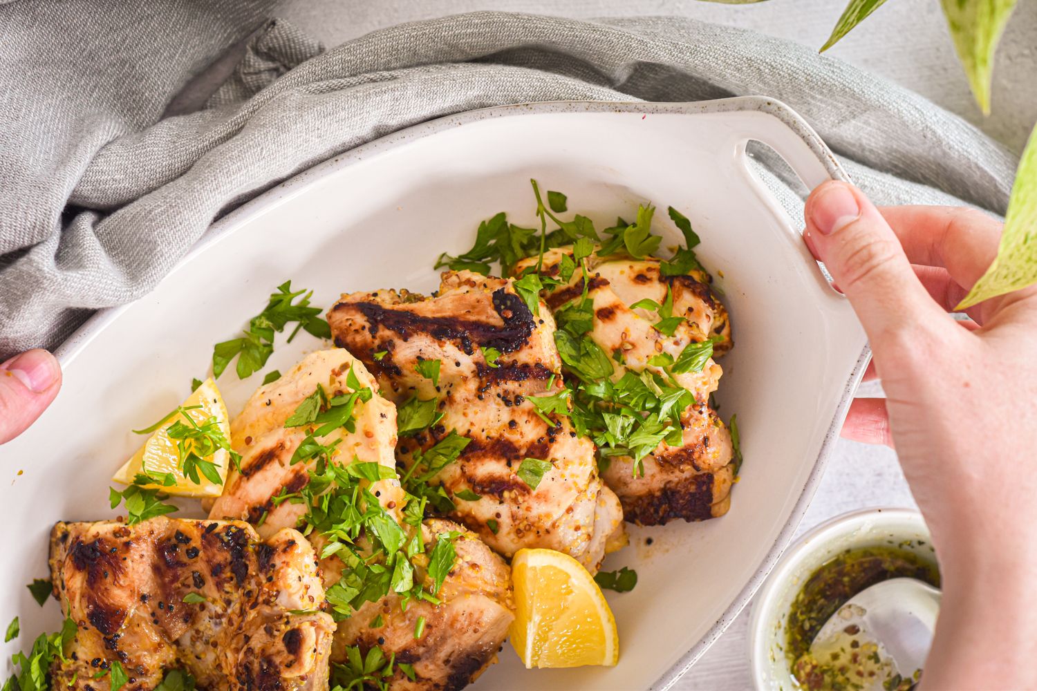 Chicken thighs that were grilled with  lemon, Dijon mustard, and garlic in a white ceramic dish.