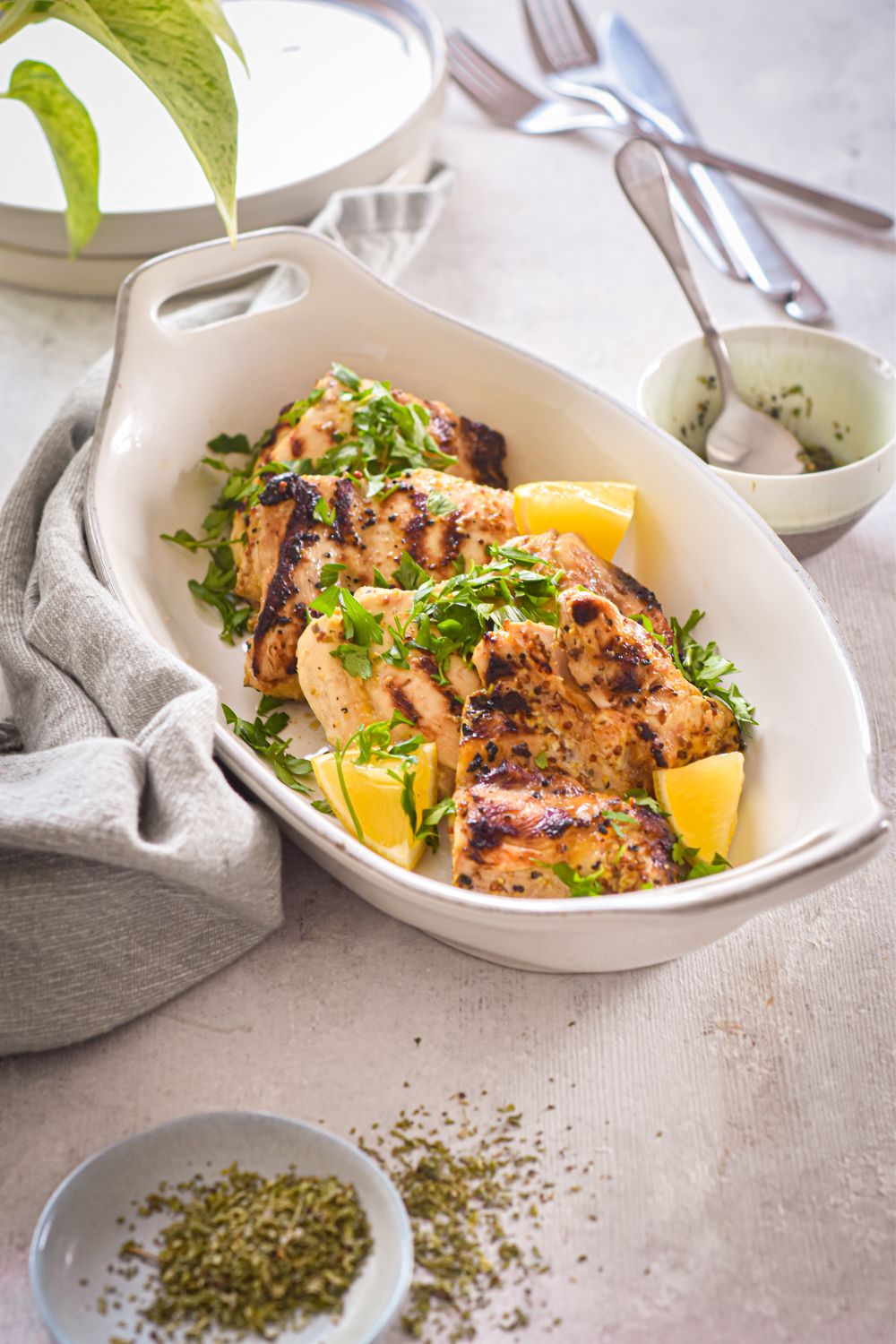 Grilled chicken thighs with Dijon mustard, garlic, and lemon in a dish with herbs on the side.