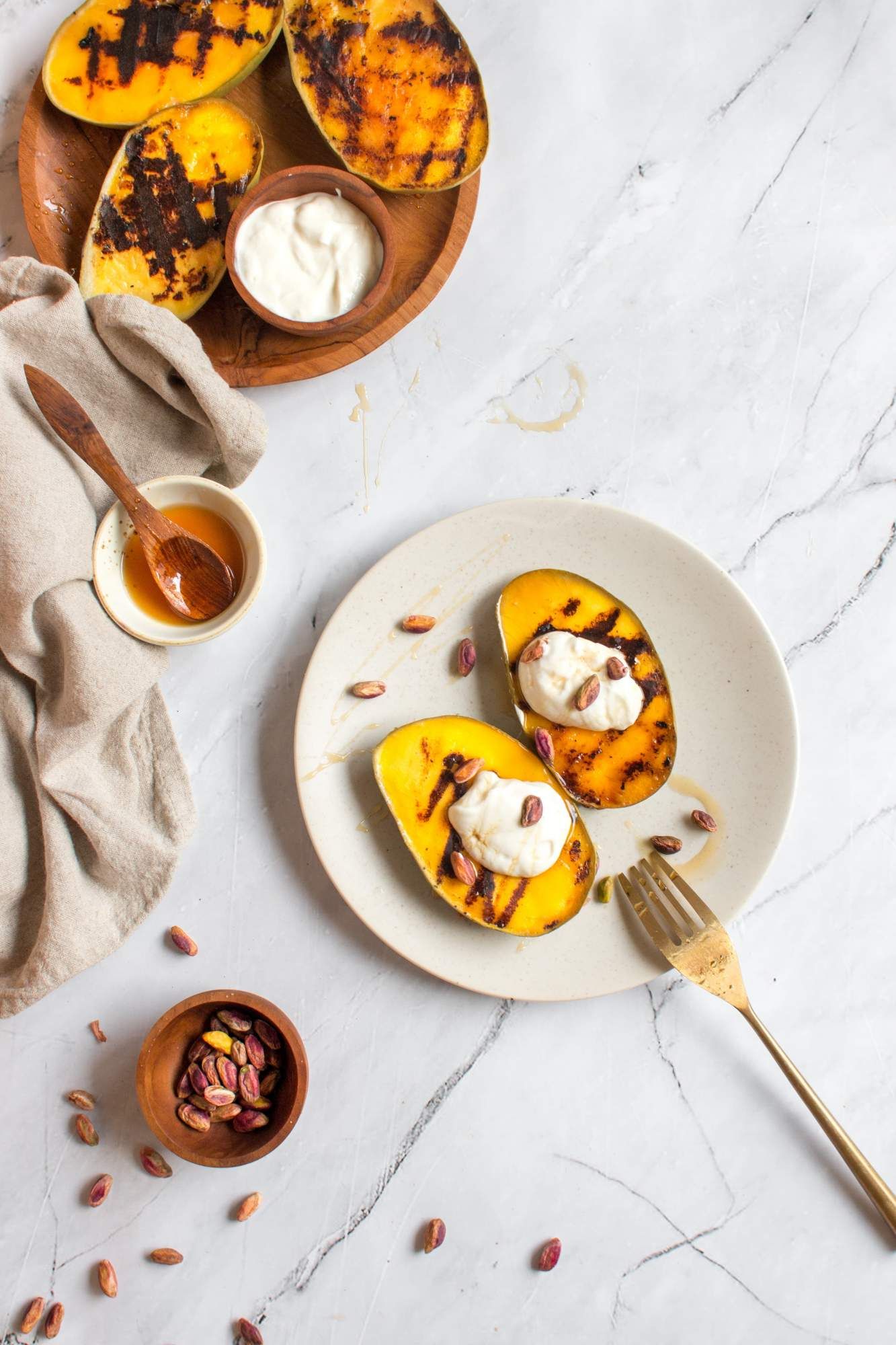 Mangoes that have been grilled with honey, pistachios, and yogurt on a plate with a brown napkin.