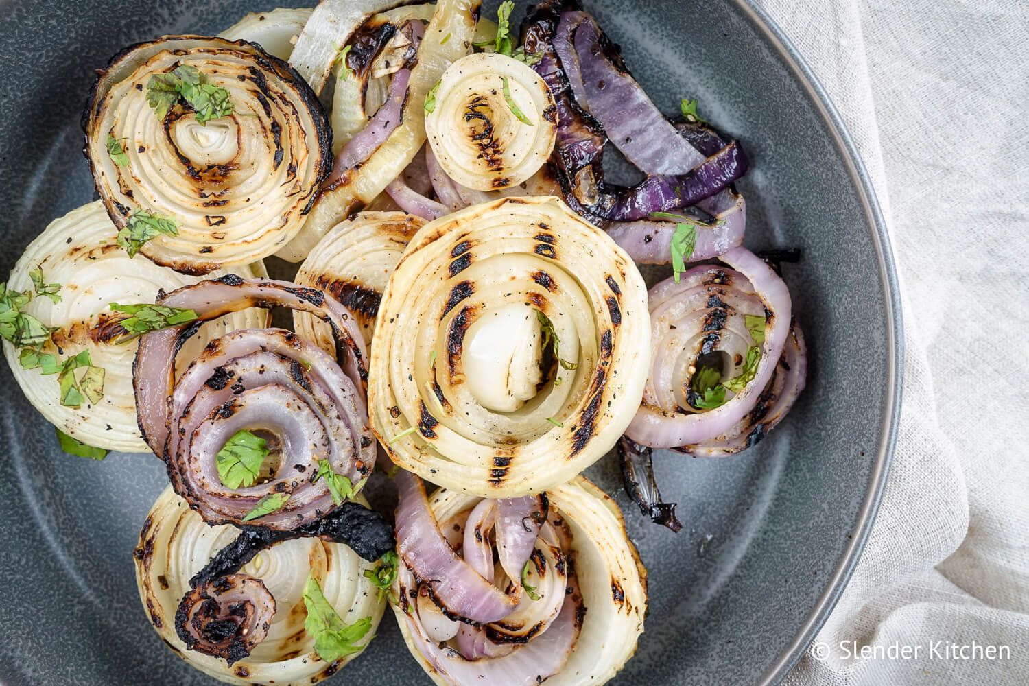 Grilling onions with olive oil, salt, and pepper on a ceramic plate with parsley.