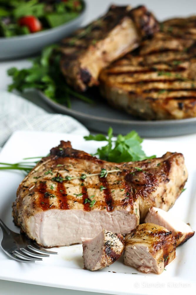 Grilled bone in pork chops with fresh thyme sliced with a knife and fork.