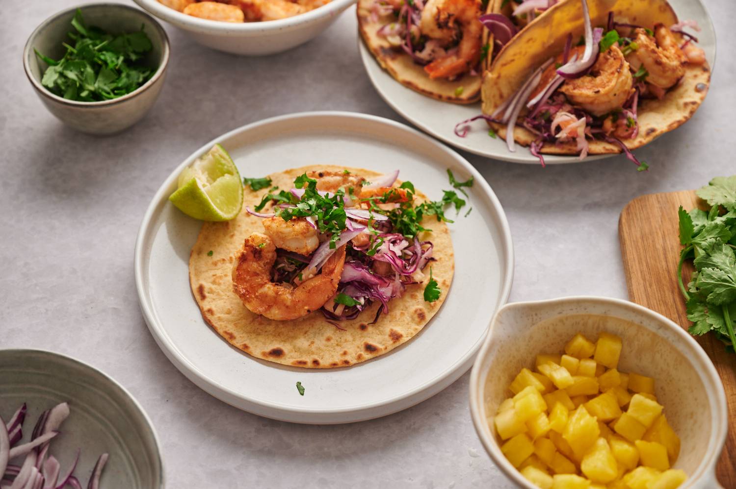 Grilled shrimp served in corn tortillas with a lime wedge, cilantro, cabbage slaw, and pineapple.