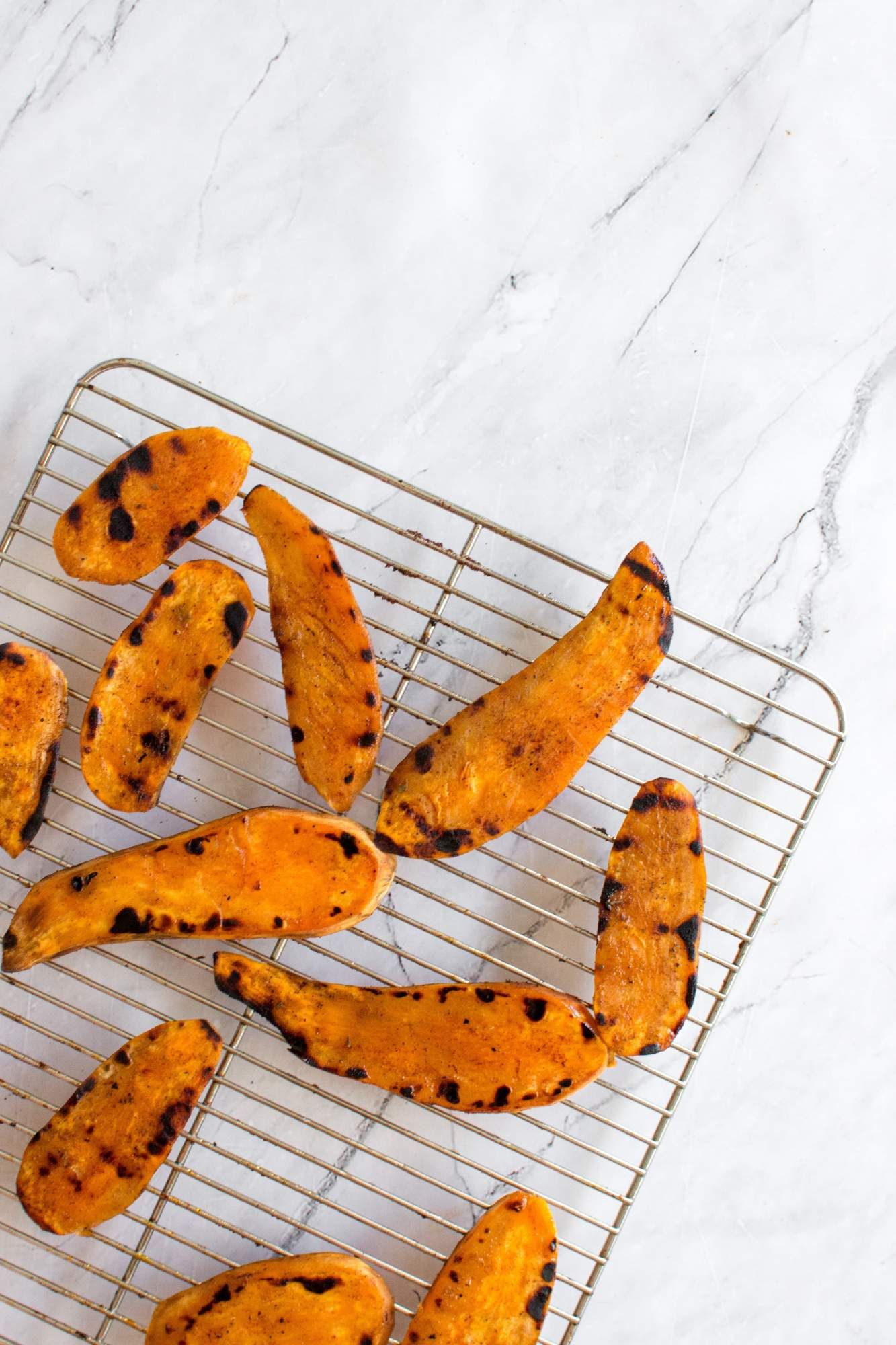 Grilling sweet potatoes with olive oil, salt and pepper on a wire rack with grill marks.