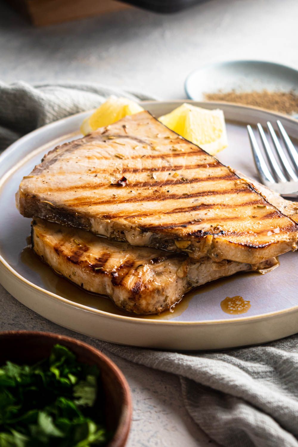 Swordfish grilled with herbs and garlic on a plate with fresh lemon on the side.