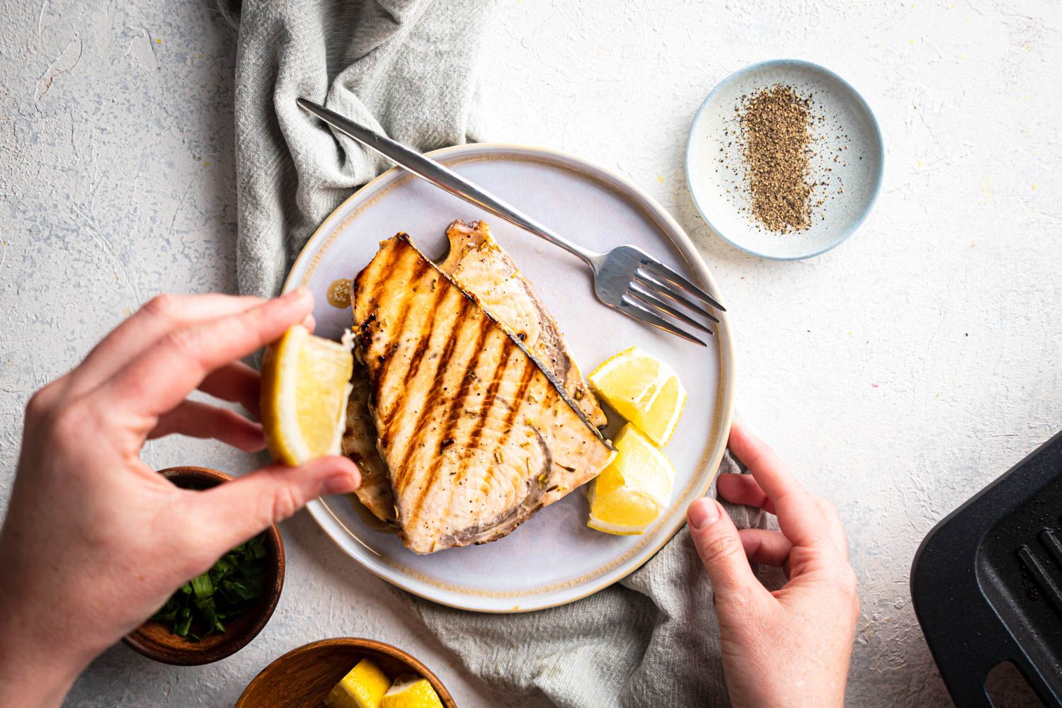 Grilled lemon swordfish steaks with garlic, pepper, and herbs served on a plate with fresh lemon slices.