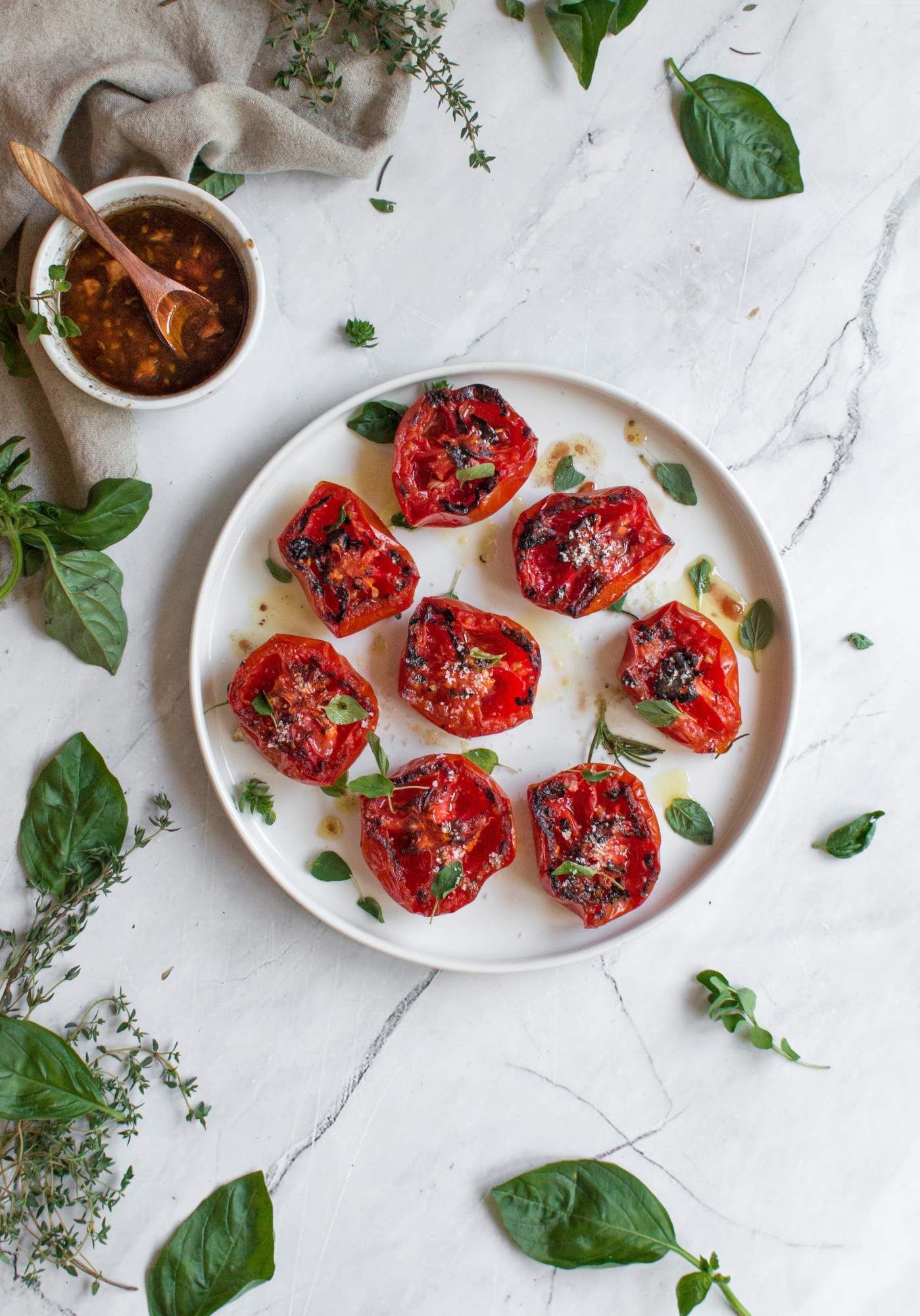 Tomatoes that have been grilled on a plate with balsamic vinegar, olive oil, salt, pepper, and basil.