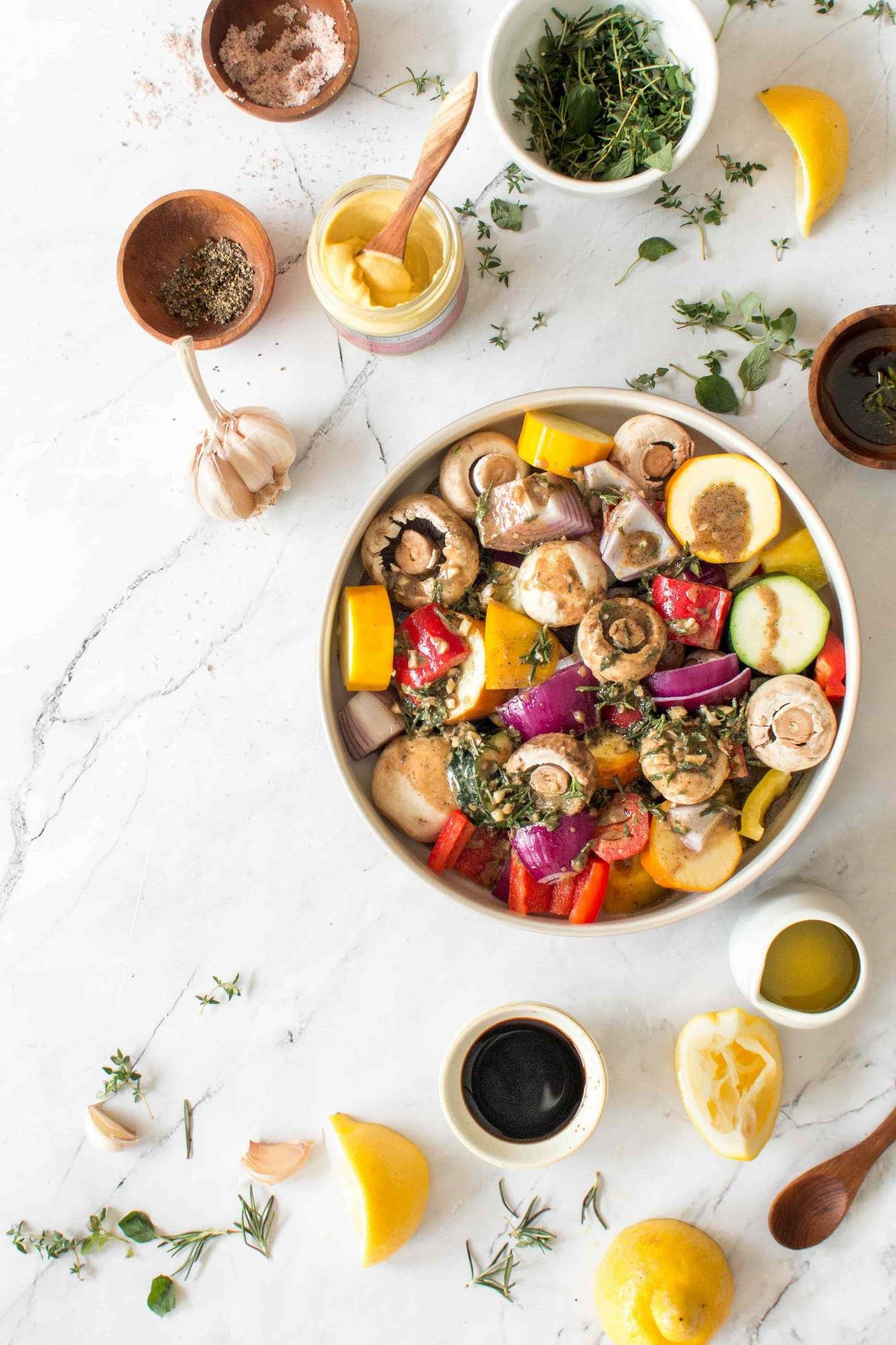 Grilled vegetable kabobs in a bowl with olive oil, lemon, fresh herbs, garlic, and Dijon mustard.