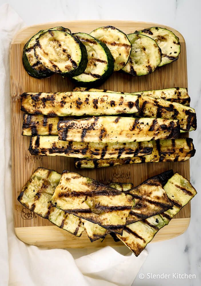 Grilled zucchini in various shapes on a wooden cutting board.