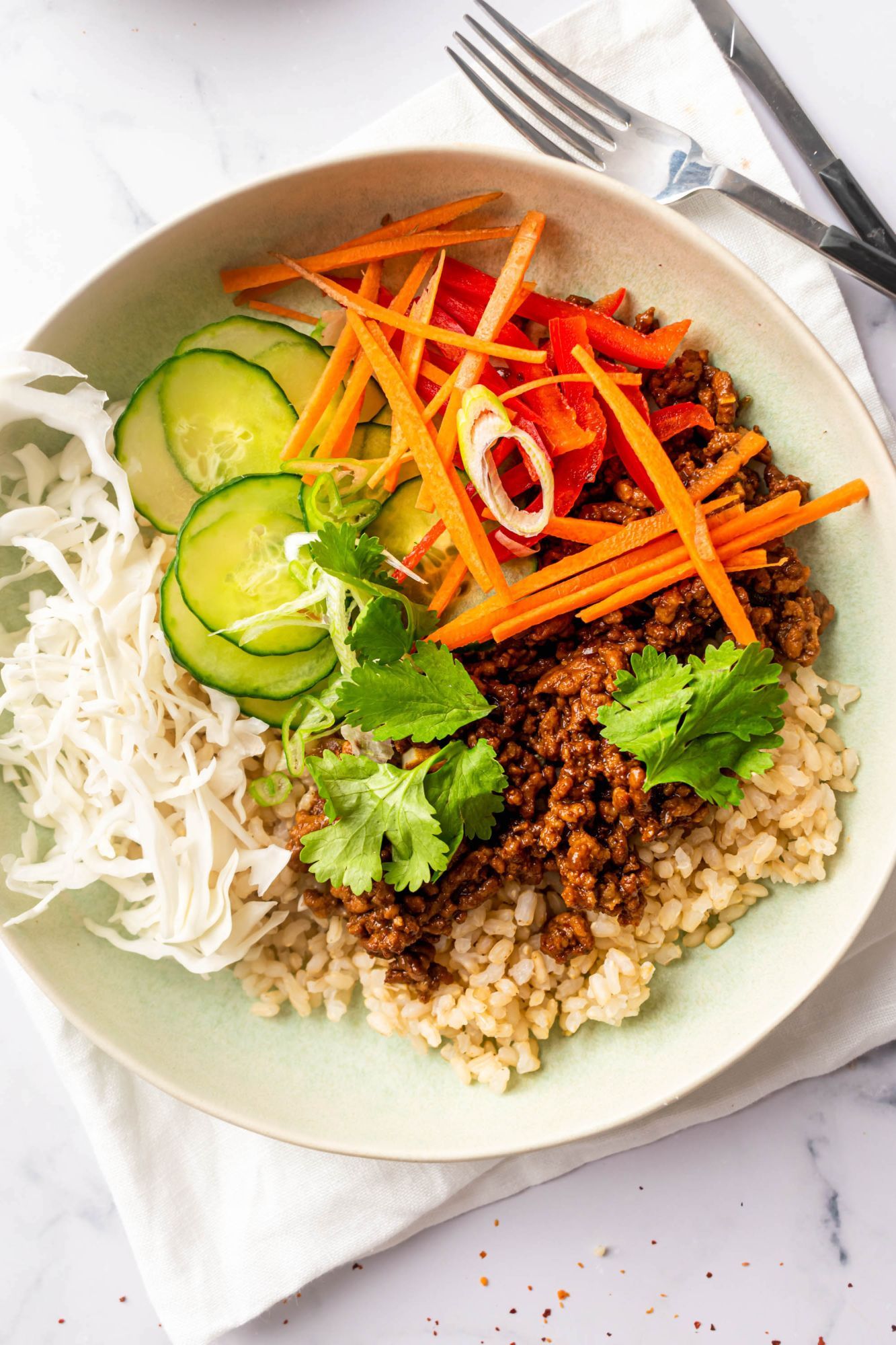 Korean beef blugogi in a bowl with brown rice, cabbage, cucumbers, carrots, and red peppers.