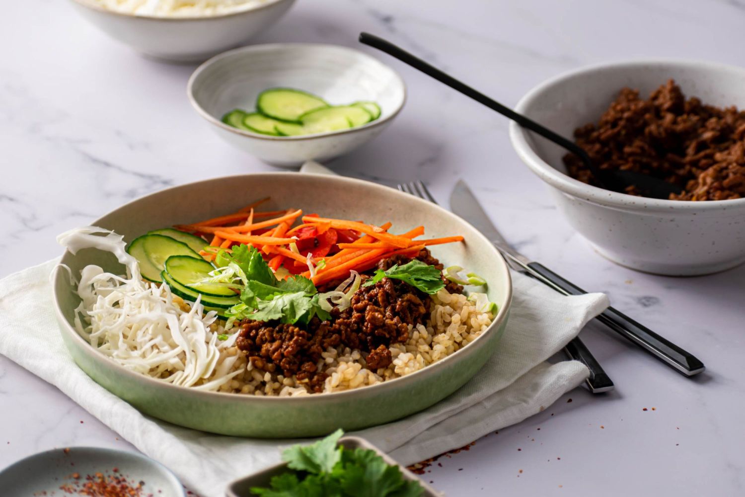 Ground beef bowls with Korean bulgogi sauce in a bowl served with steamed rice, fresh cilantro, and vegetables.