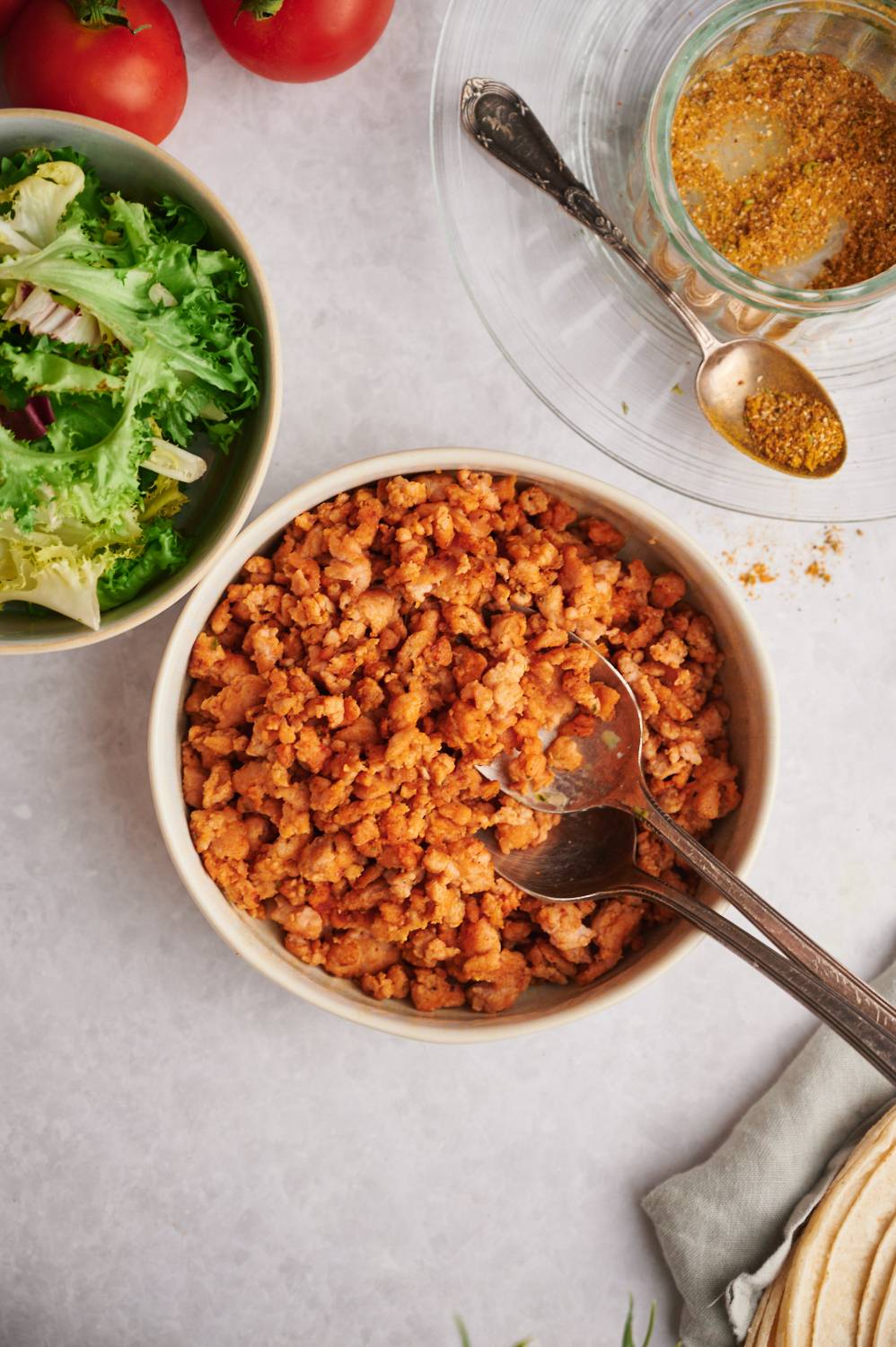 Taco seasoned ground chicken in a bowl with homemade seasoning, lettuce, and tomatoes on the side.