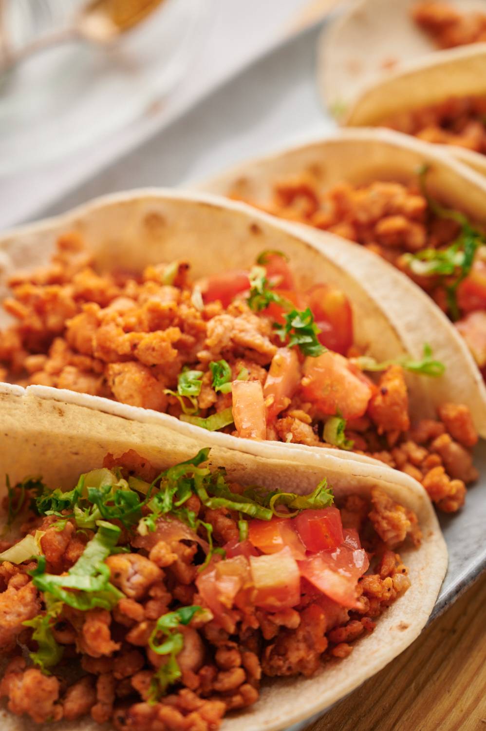 Flour tortillas filled with ground chicken taco meat, tomatoes, and lettuce on a white plate.